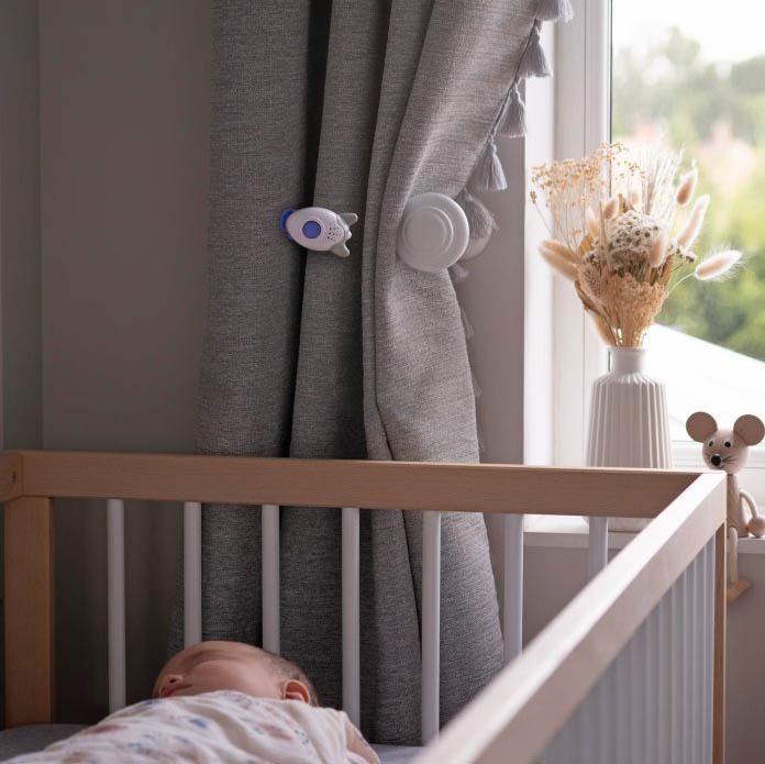 Wooshh pink noise gadget in a baby's bedroom attached to the curtain above sleeping baby